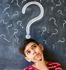 Kids stands in front of chalkboard with question marks written across it