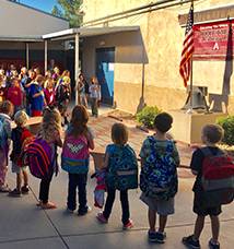 Students and teachers recite the pledge of allegiance in front of an American flag outside