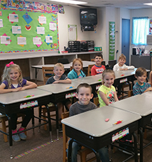 Two rows of smiling students sit behind their desks